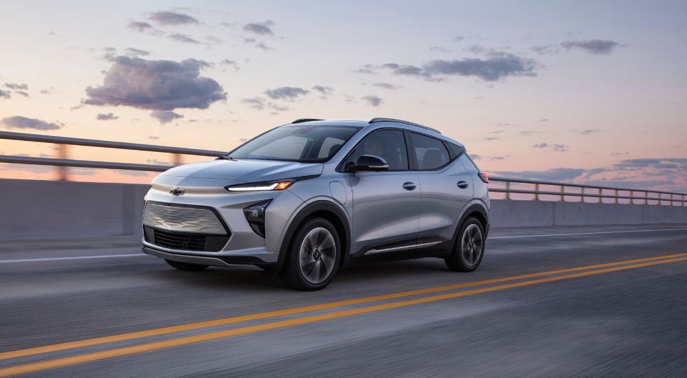 A silver 2022 Chevy Bolt EUV driving across a bridge at sunset.