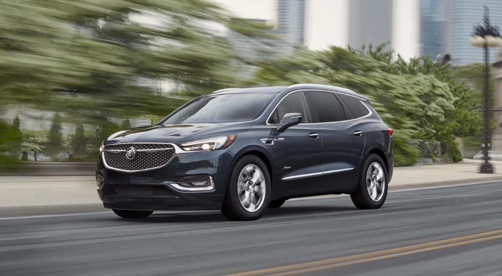 A dark gray 2021 Buick Enclave Avenir speeding down a tree-lined city street.