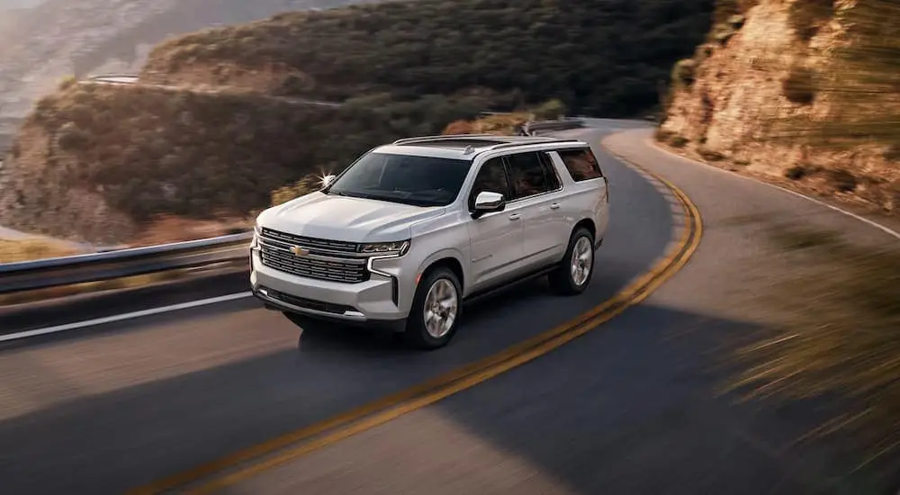 A silver 2022 Chevy Suburban LT is shown driving on a winding highway.