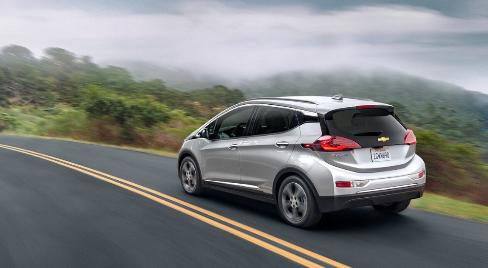 A silver 2019 Chevy Bolt EV is shown driving on a winding road.