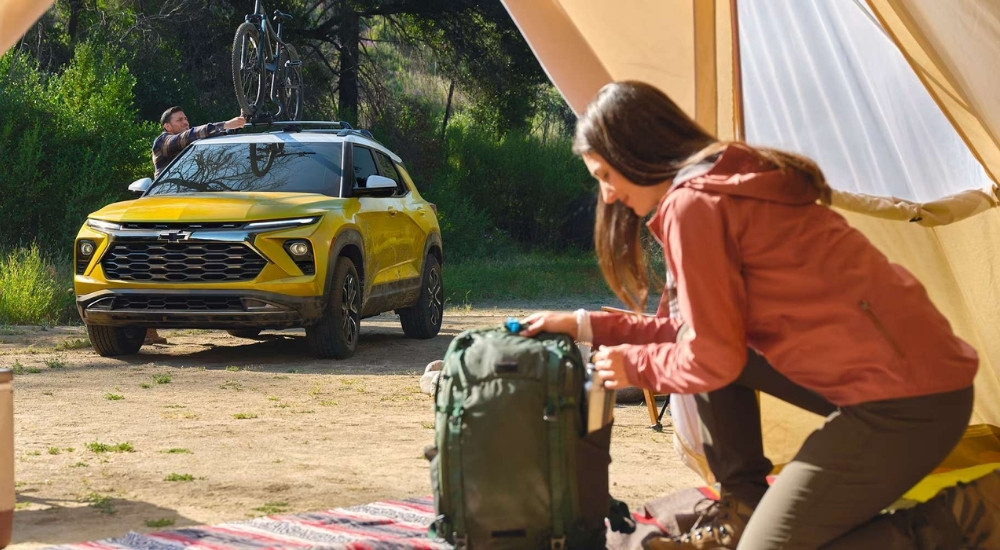 A yellow 2025 Chevy Trailblazer ACTIV parked off-road by a campsite.