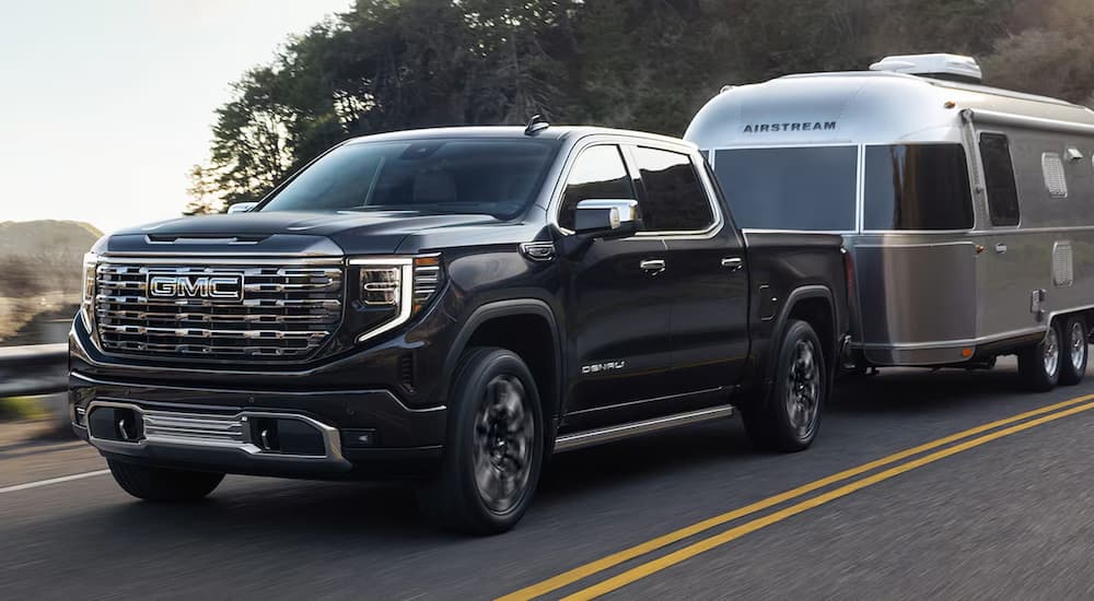 Black 2025 GMC Sierra 1500 Denali towing a silver camper.
