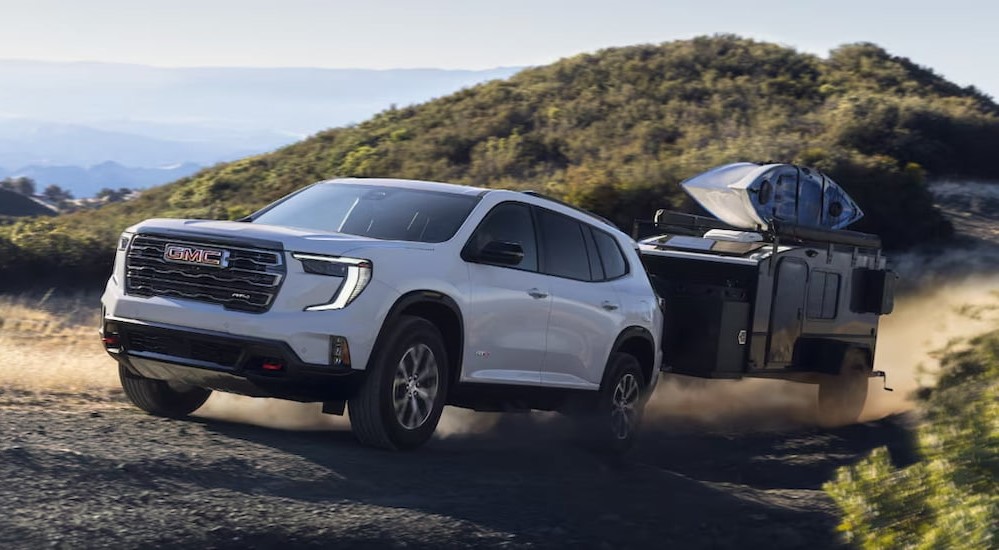 A white 2025 GMC Acadia AT4 towing a trailer.