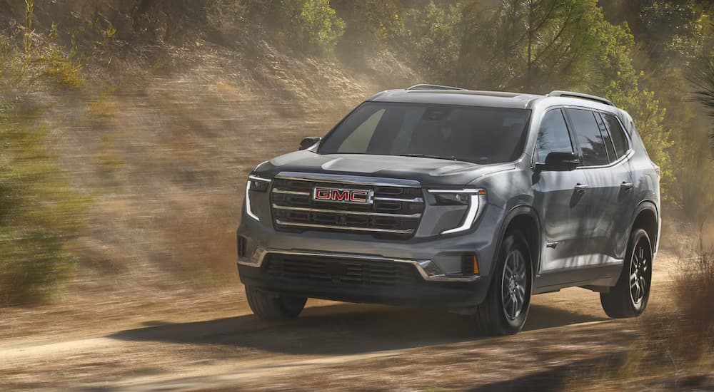 Grey 2025 GMC Acadia for sale driving down a dirt road.