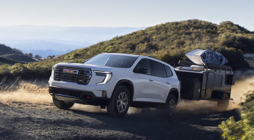 White 2025 GMC Acadia AT4 towing a camper on a rocky road.
