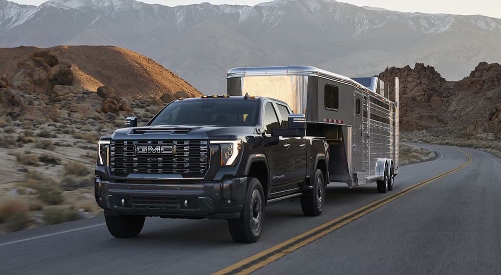 Black 2025 GMC Sierra 2500 HD towing a trailer down a road.