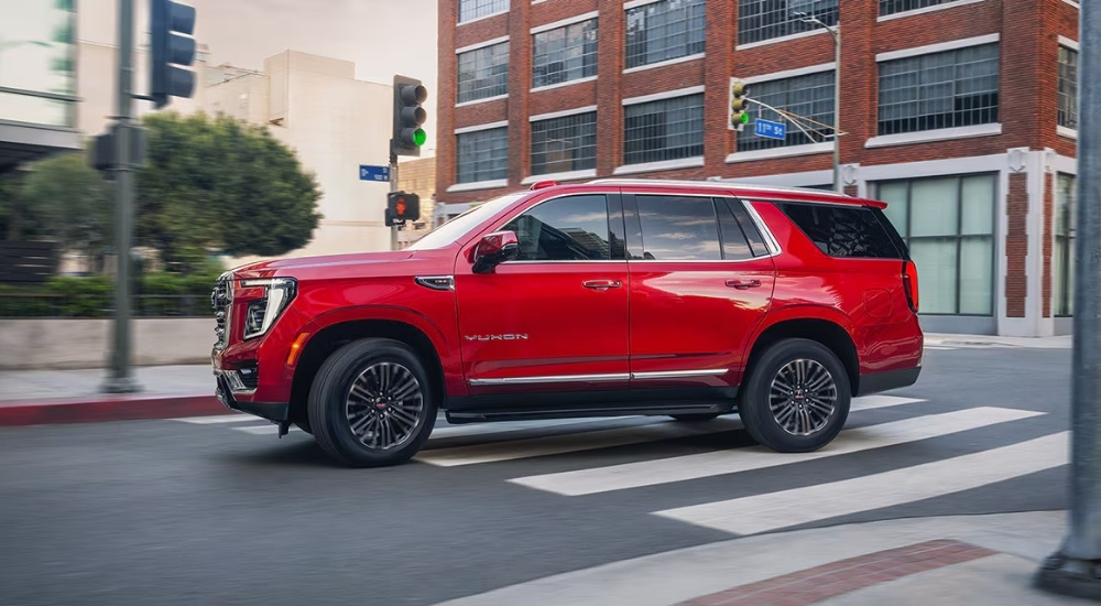A red 2025 GMC Yukon for sale in Corinth driving through an intersection.