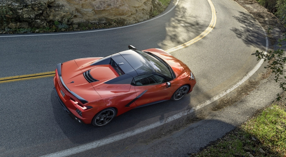 An orange 2020 Chevy Corvette Stingray is shown driving on a tree-lined road.