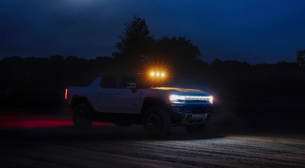A white 2022 GMC Hummer EV Pickup driving at night after visiting an electric car dealership in MS.