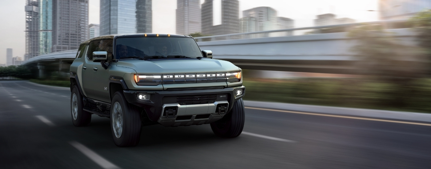A green 2022 GMC Hummer EV is shown driving past skyscrapers.