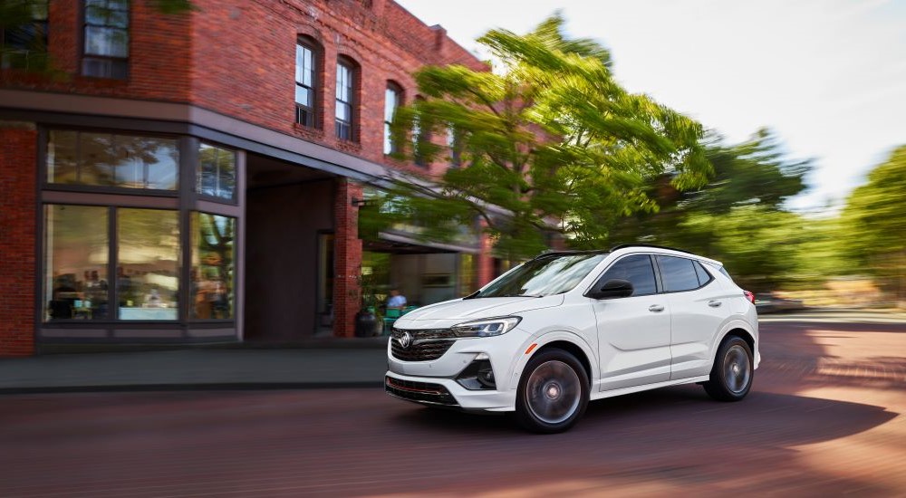 A white 2022 Buick Encore GX driving past a brick building.