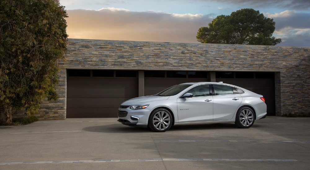 A silver 2017 Chevy Malibu is shown parked outside of a garage.