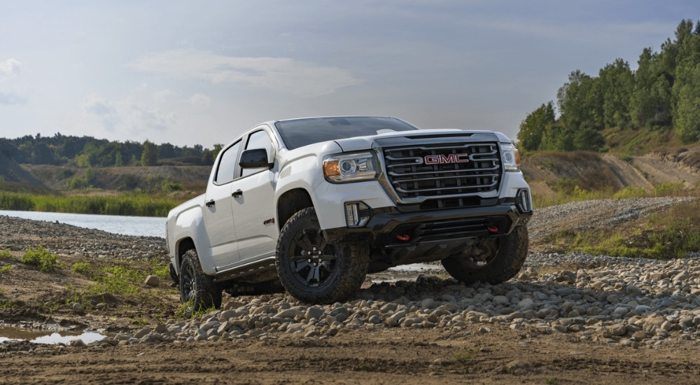 A white 2021 GMC Canyon AT4 is shown off-roading on a path near a river.