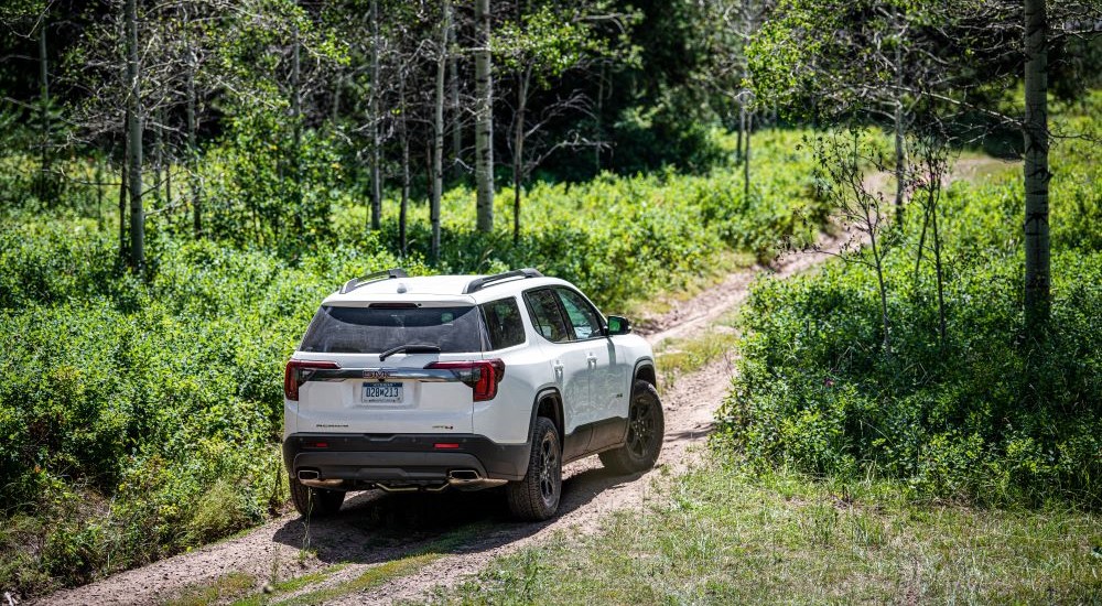 A white 2020 GMC Acadia AT4 is shown from the rear on a trail.
