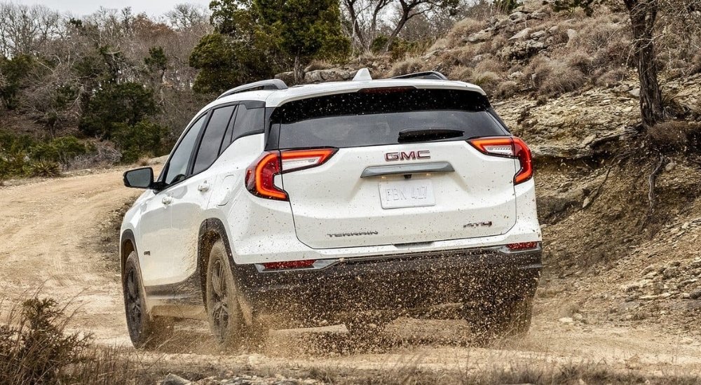 A black 2024 GMC Terrain AT4 is shown from the rear driving to a New Albany GMC dealer.