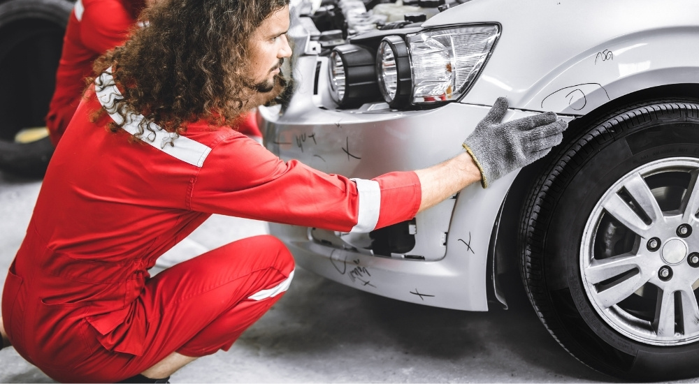 A technician is looking at body damage on a silver 2014 Chevy Sonic.