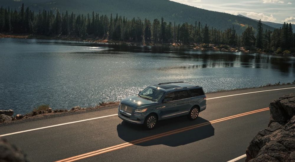 A green 2023 Lincoln Navigator is shown driving past a lake.
