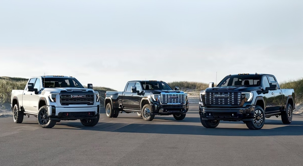 A white 2025 GMC Sierra 2500 HD AT4X, a black 3500 HD Denali, and a black 2500 HD Denali Ultimate parked on pavement