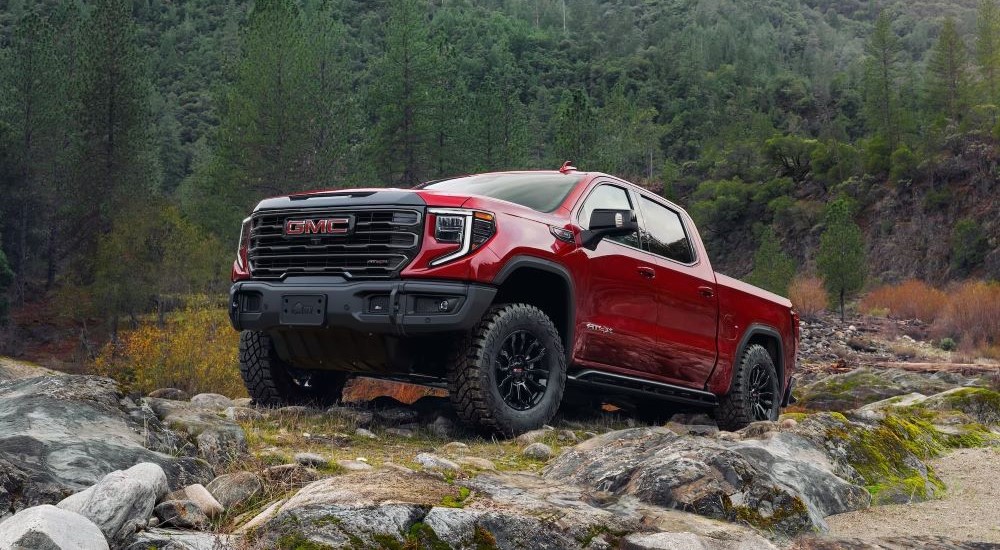 A red 2025 GMC Sierra 1500 AT4X is off-roading on a rocky trail.