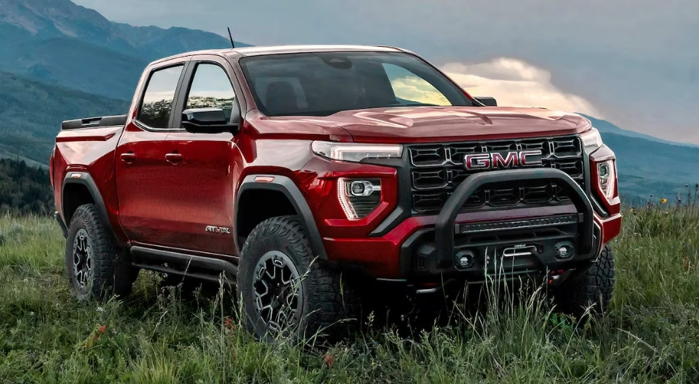 A red 2025 GMC Canyon AT4X parked offroad on a grassy hillside.