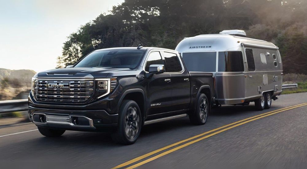 Black 2025 GMC Sierra 1500 Denali towing a silver camper.