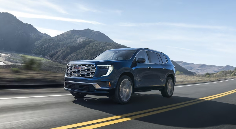 A blue 2025 GMC Acadia for sale driving on a highway.