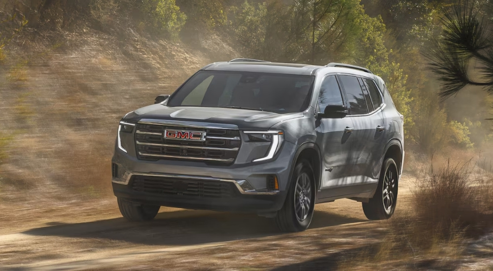 Grey 2025 GMC Acadia for sale driving down a dirt road.