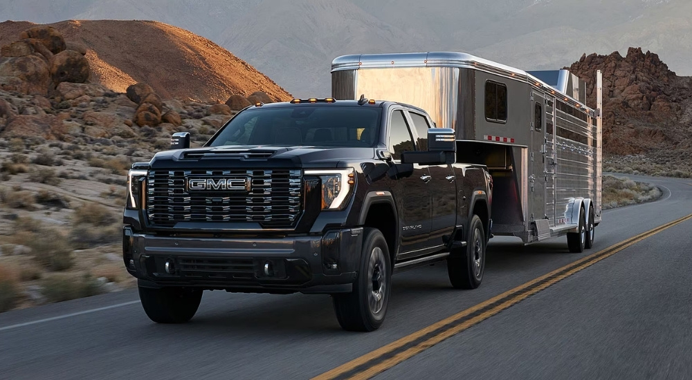 Black 2025 GMC Sierra 2500 HD towing a trailer down a road.