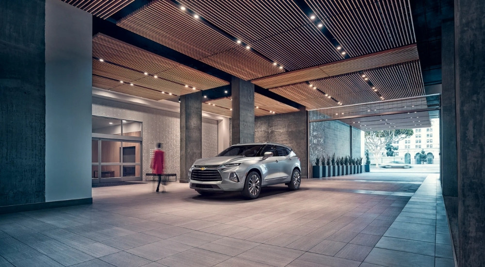 A silver 2019 Chevy Blazer Premier is shown parked in front of a hotel.