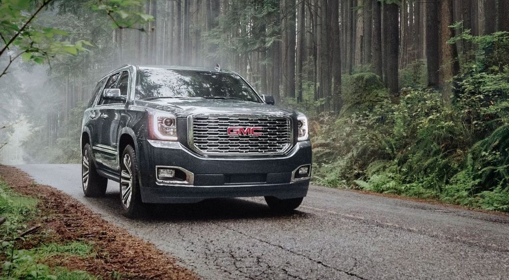 A grey 2020 GMC Yukon Denali is shown driving on a tree-lined road.