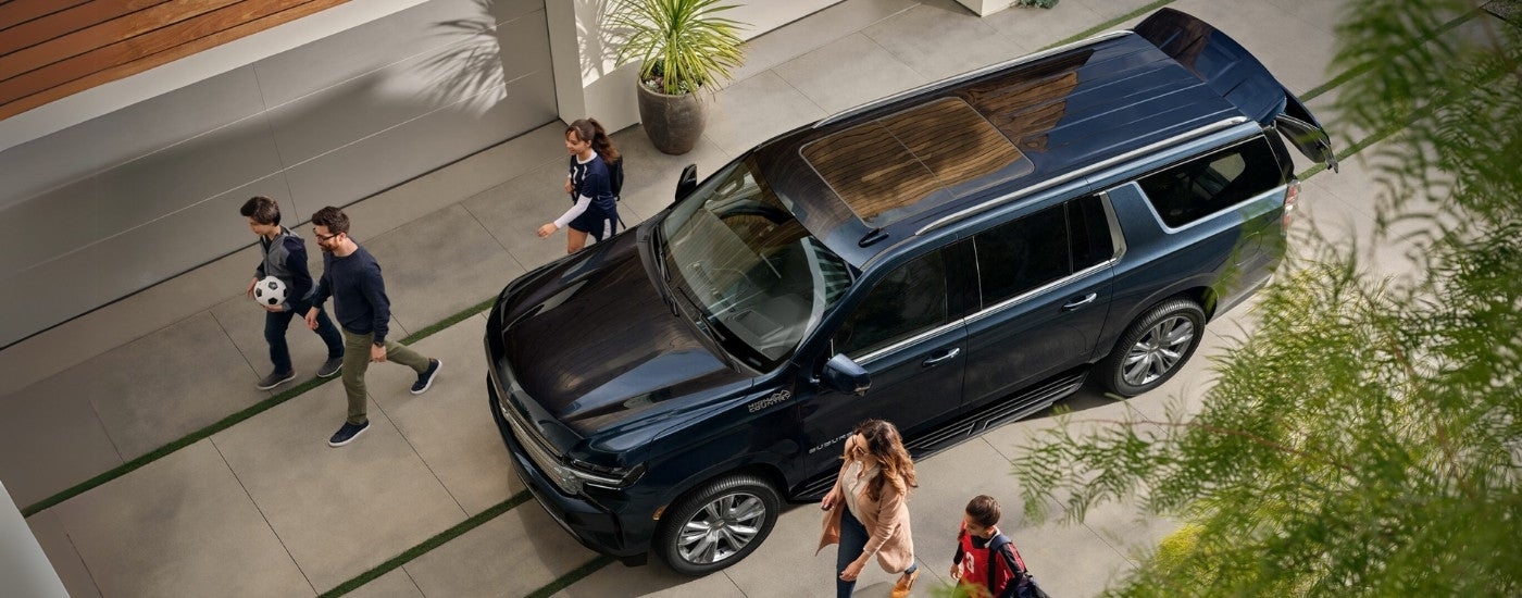 A dark blue 2023 Chevy Suburban High Country is shown parked near a Booneville Chevy dealer.