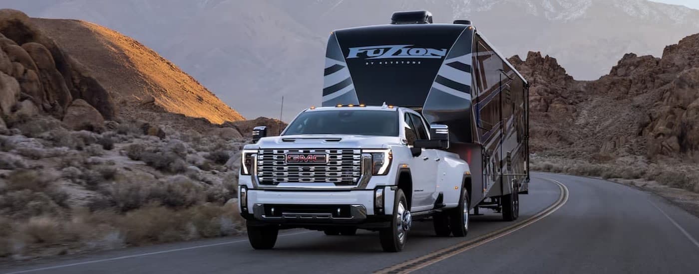 A white 2025 GMC Sierra 2500 HD Denali towing a trailer.