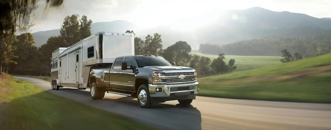 A dark grey 2016 Chevy Silverado 3500 HD towing a camper past fields on sunny day.
