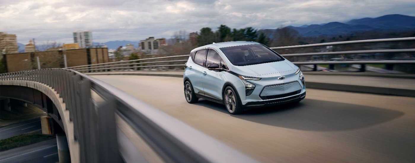 A silver 2023 Chevy Bolt EV is driving over a bridge.