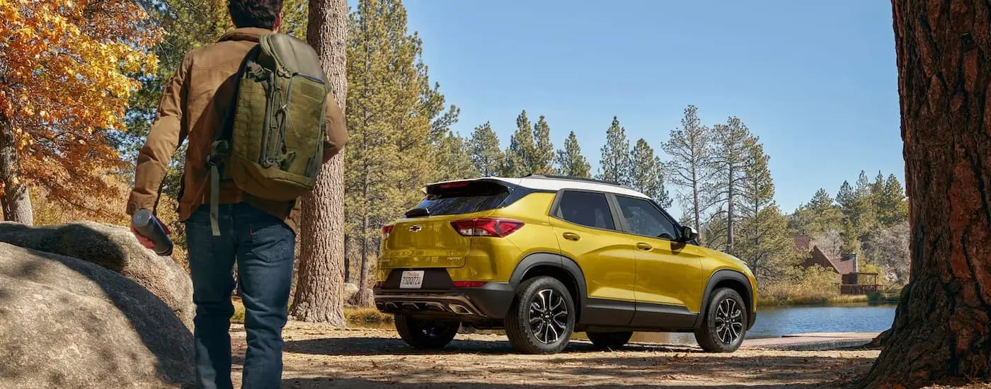  A gold 2023 Chevy Trailblazer is shown from a rear angled parked near a hiking trail and lake.
