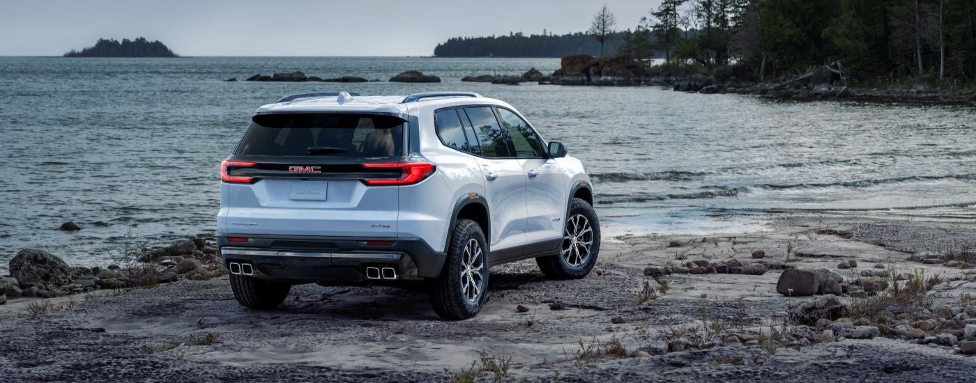 Rear view of a white 2024 GMC Acadia AT4 parked on a lake shore.