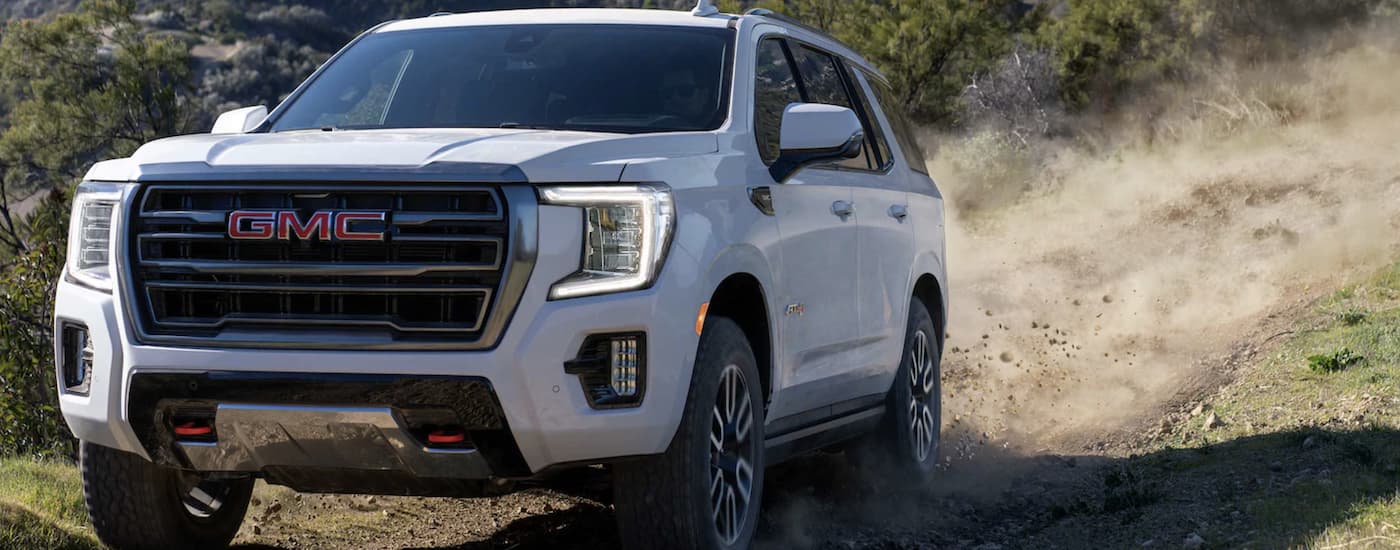 White 2023 GMC Yukon AT4 driving down a dirt road.