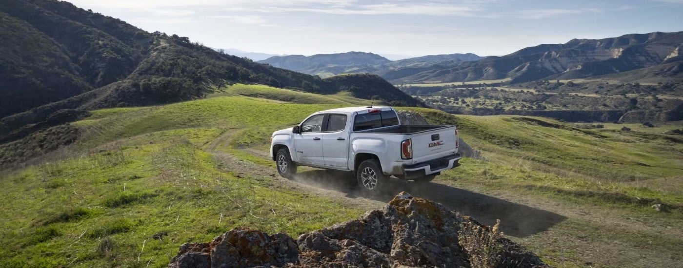 A white 2022 GMC Canyon AT4 is shown from the rear driving on a mountain path.