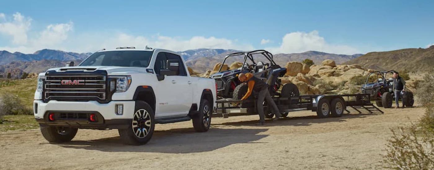 A white 2020 GMC Sierra 3500HD is shown from the front at an angle while towing a UTV.