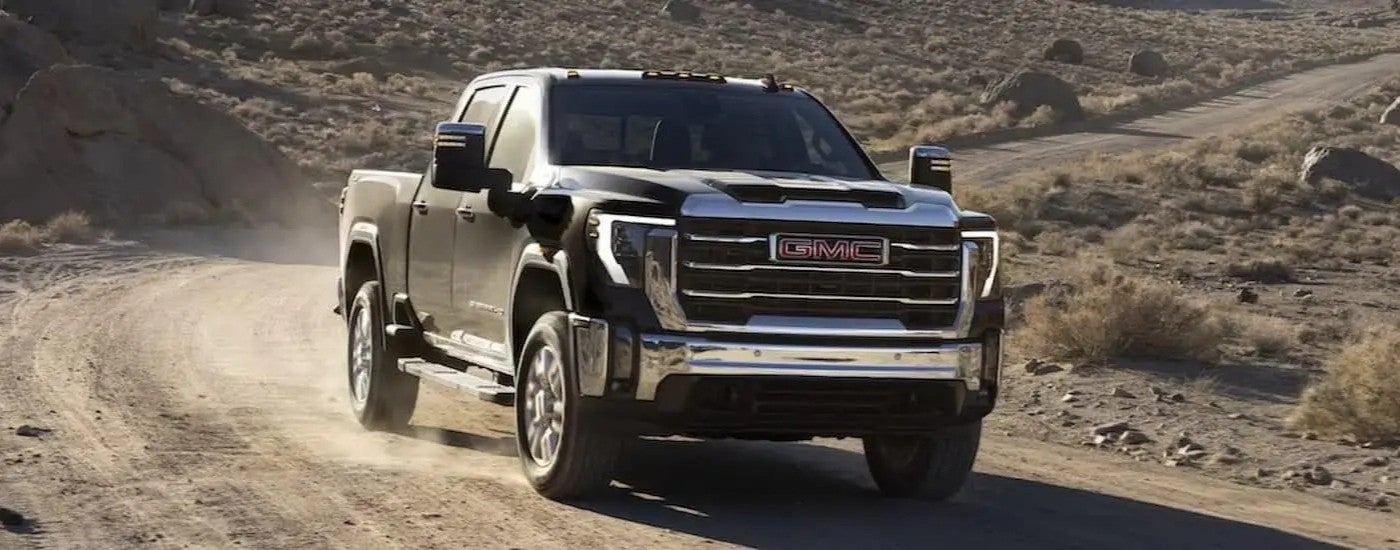 One of the most popular GMC trucks for sale, a black 2024 GMC Sierra 2500 HD, is shown driving off-road.