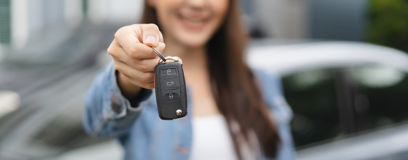 Woman holding out a car key at a car dealership