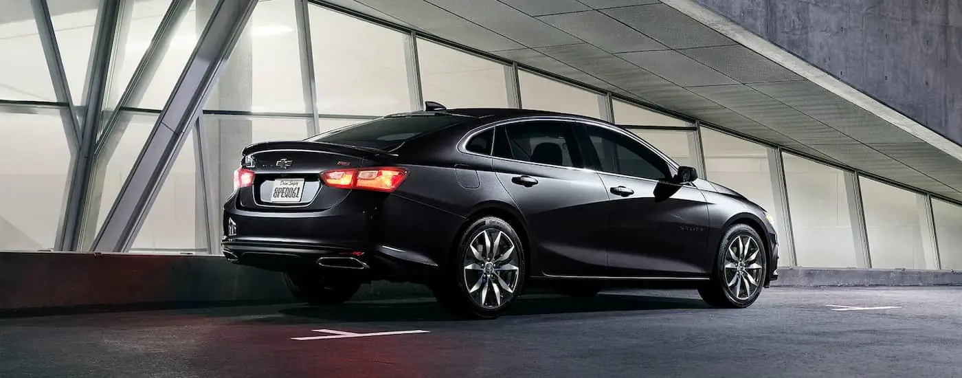 A black 2023 Chevy Malibu RS is shown from a rear side angle next to a building.