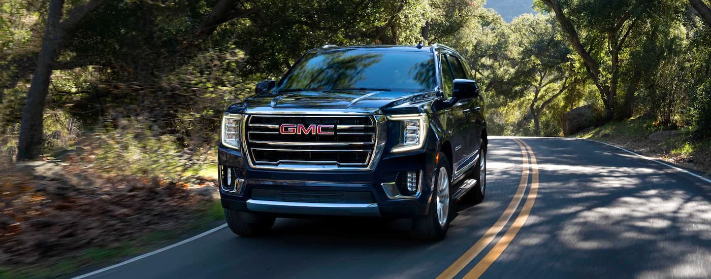 A black 2022 GMC Yukon from the front driving down a tree-lined road near Selmer