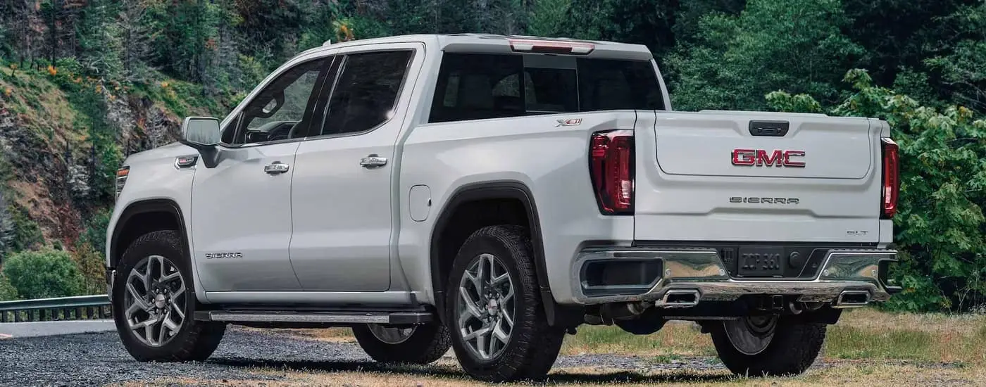  A white 2023 GMC Sierra 1500 SLT is shown from a rear angle parked next to a road.