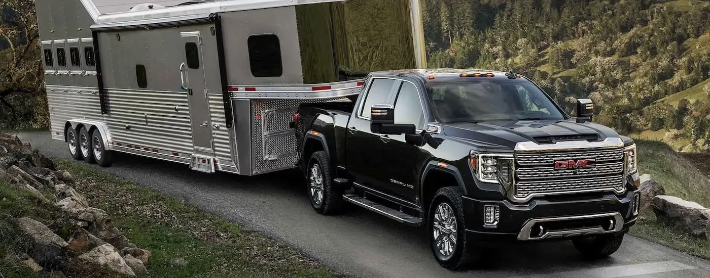 A red 2023 GMC Sierra 2500 HD Denali is shown towing a large silver trailer up a hill.
