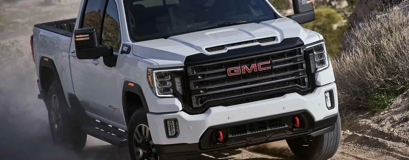 A white 2023 GMC Sierra 3500 AT4 for sale is shown driving on a dusty dirt road.