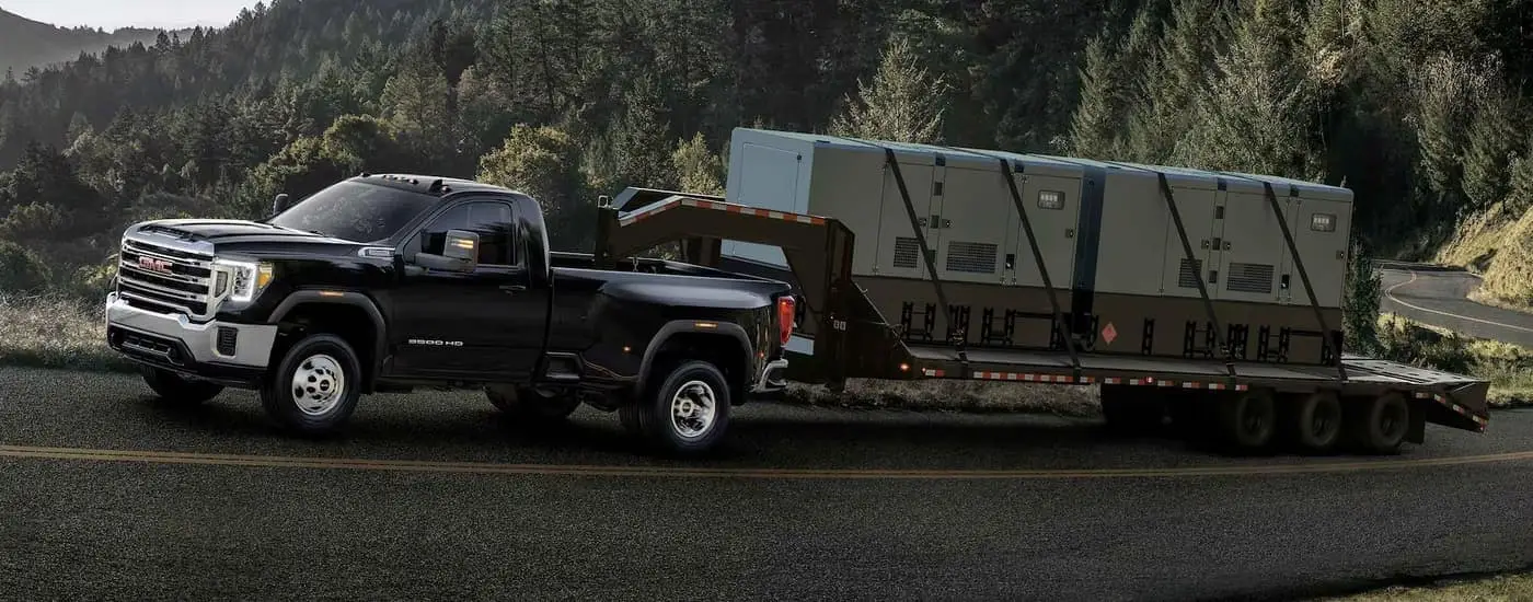 A black 2023 GMC Sierra 3500 HD is shown towing heavy cargo up an incline.