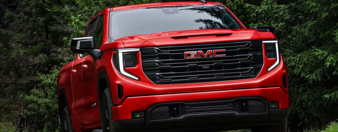A red 2023 GMC Sierra 1500 Elevation for sale is shown from the front driving on a dirt road.