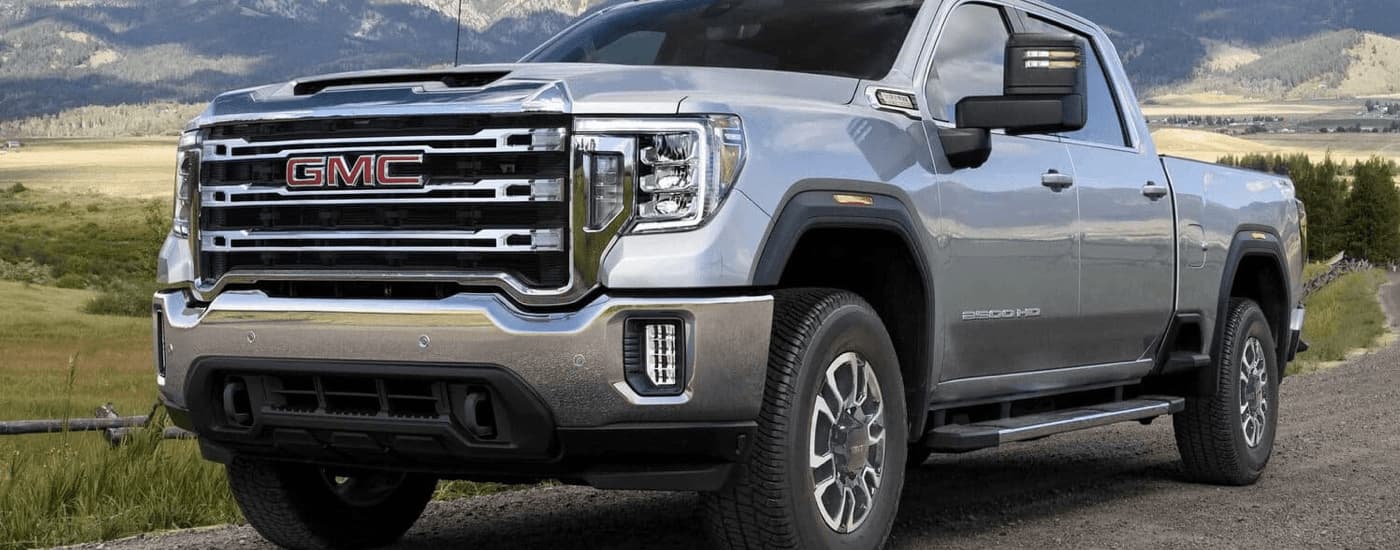 A silver 2023 GMC Sierra 2500 HD SLE for sale is shown driving on a road through an open field.