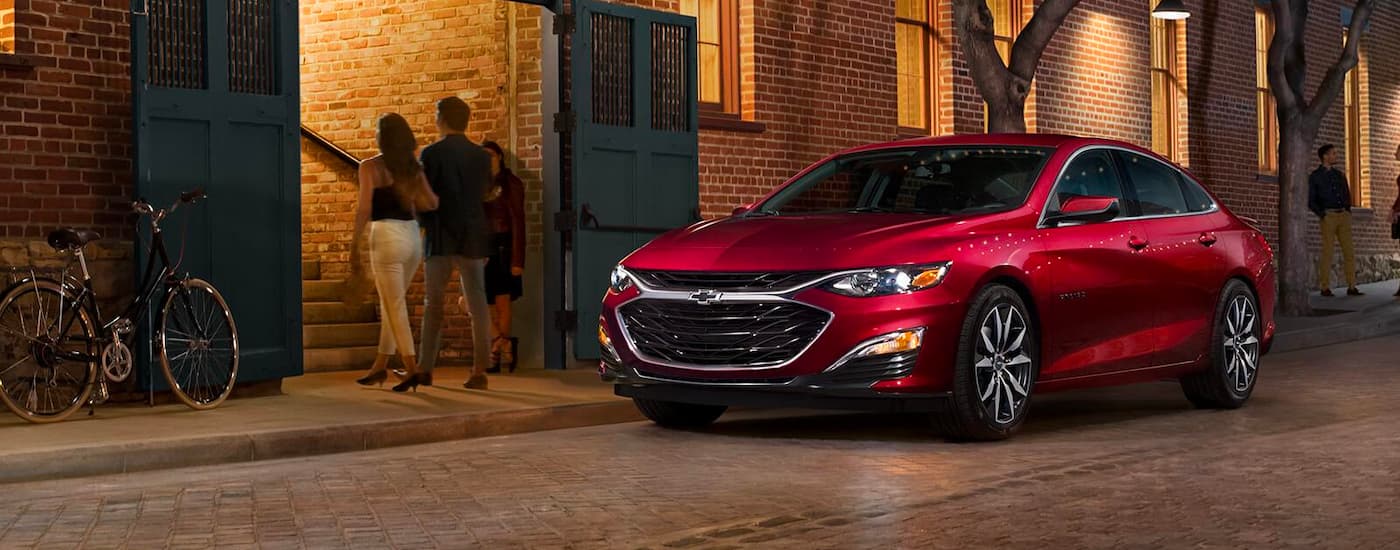 A red 2023 Chevy Malibu is shown on a city street after leaving a Tupelo used car dealer.